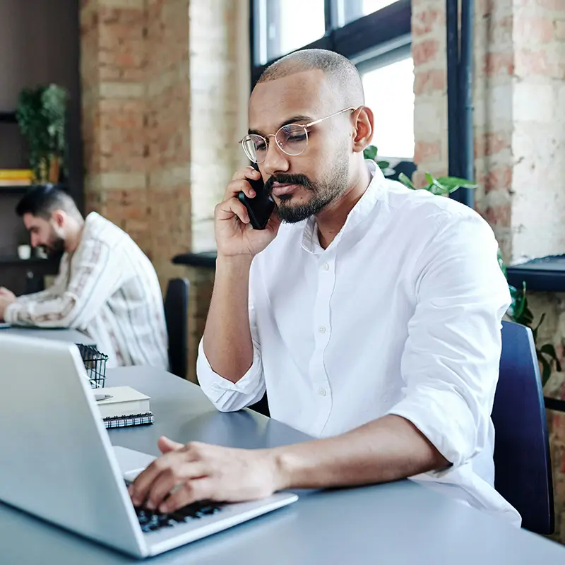 a business person is sitting at a desk with their laptop, while also on the phone